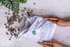 Dark clay balls spilling out of hand held Foliage Therapy calico bag next to plant
