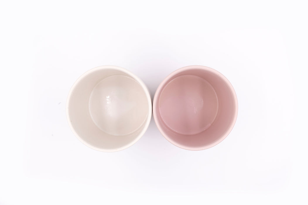 Top view of two ceramic plant pots with no drainage holes, one pink the other white